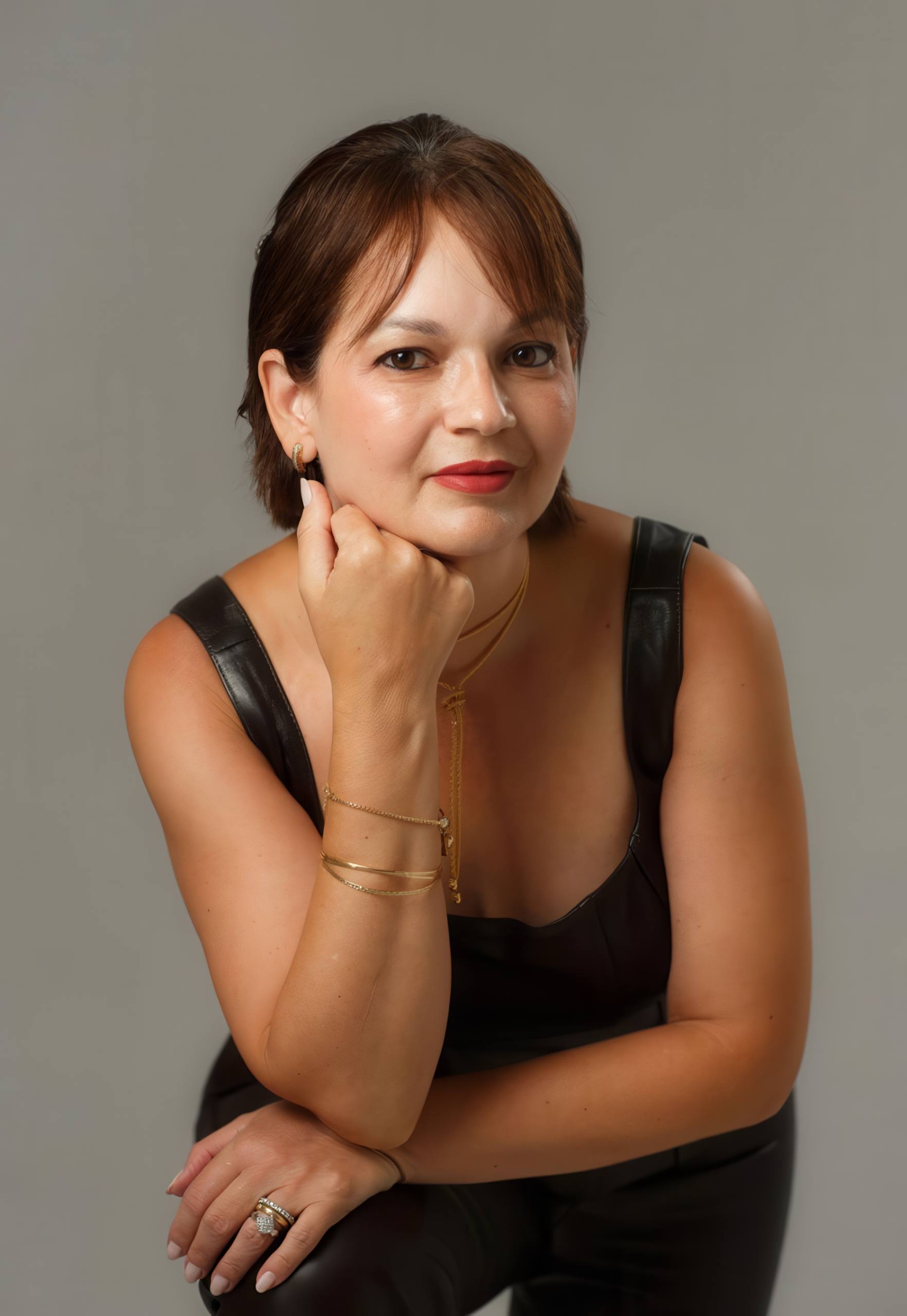 Dra. Yanne Batista em retrato próximo, de preto, com a mão no queixo.